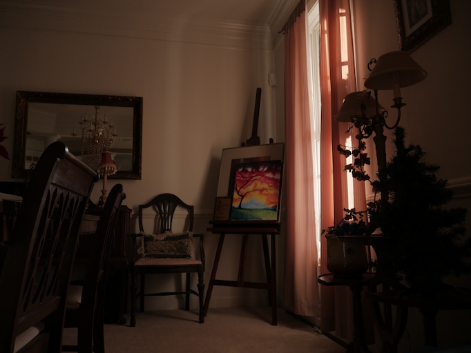 An easel in a dining room, next to a window with red curtains.